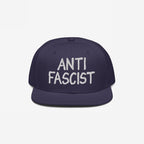 Navy-blue flat-brim snapback hat with ANTI FASCIST in white embroidery, reflecting a bold, unisex statement for those opposing fascism. Ethically made and supports ACLU.