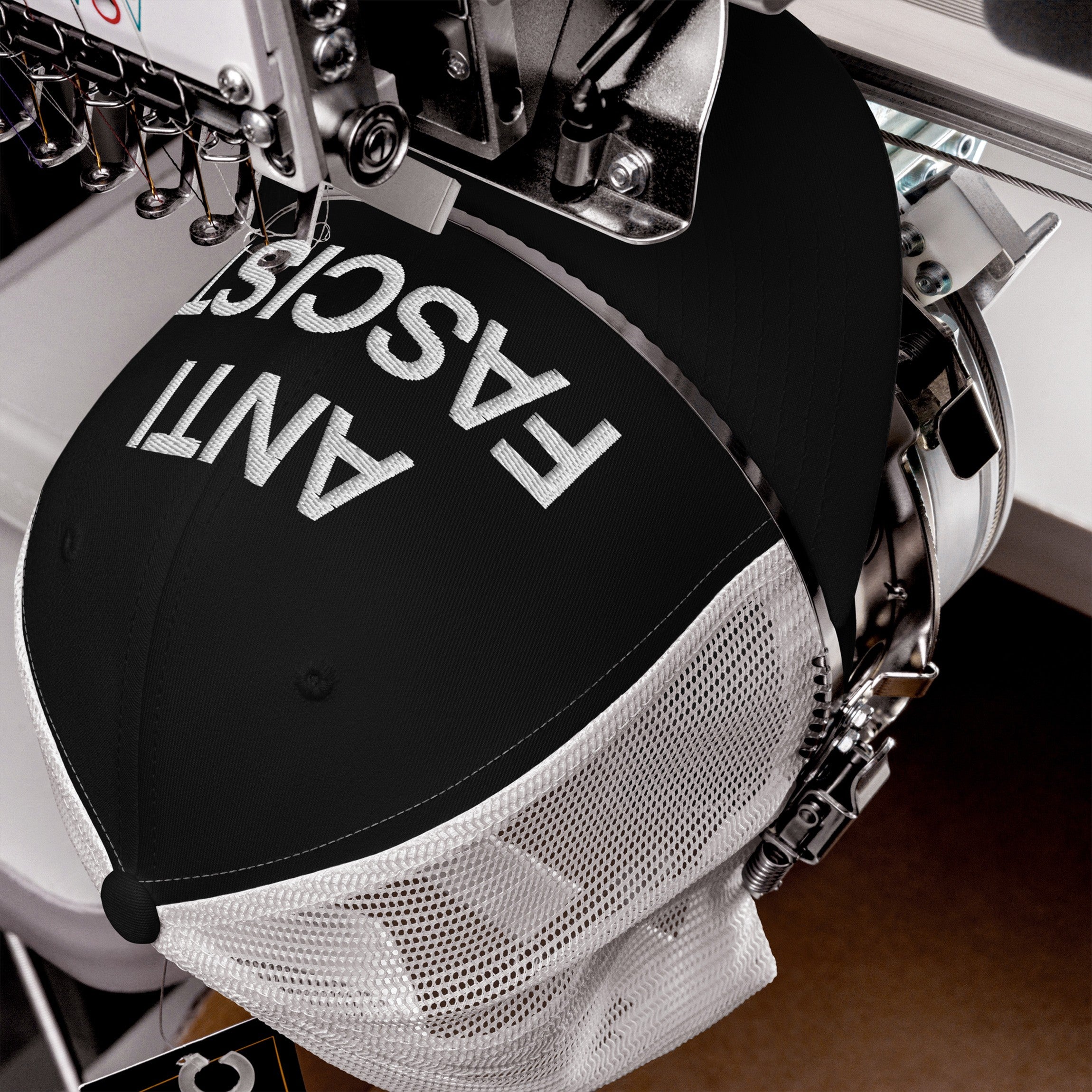 The Anti-Fascist Classic Hat in a commercial embroidery machine, featuring ANTI FASCIST stitched in white thread on the front, embodying bold resistance and timeless style.