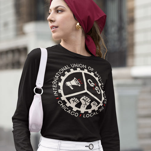 Young person models Chicago Anti-Fascist Union T-shirt with gear emblem, symbols of activism, and local text. Paired with headscarf, hoop earrings, white pants, and shoulder bag, reflecting bold, political style.