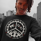 Person wearing Texas Anti-Fascist Union Hoodie with cog-wheel design featuring icons of a megaphone, broken chain, and raised fists, standing against a city skyline.