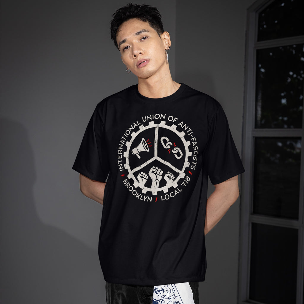 Young man wears a Brooklyn Anti-Fascist Union T-shirt, featuring a union-style graphic with a megaphone, broken chains, and raised fists. Perfect for those embracing borough pride and solidarity.