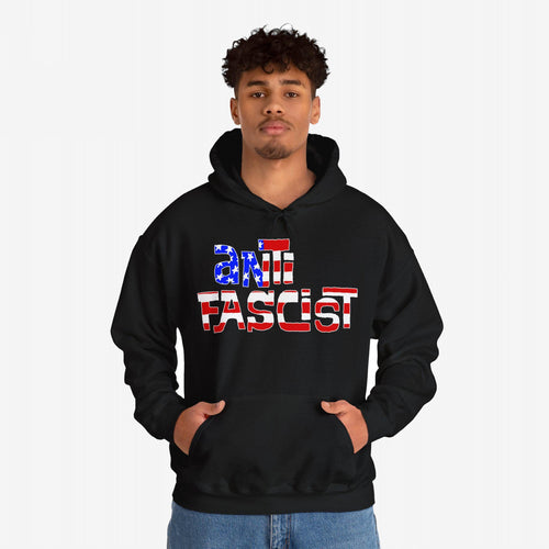 Young man wearing the Anti Fascist USA Shirt, a black hoodie featuring ANTI FASCIST with an American-flag motif, symbolizing progressive resistance and patriotism. Hands in kangaroo pocket, paired with blue jeans.