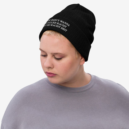 Person wearing the Anti-Racist Hat, a black knit beanie with a bold message confronting racism, paired with a light-gray crewneck. The wearer is looking down, emphasizing the hat's impactful statement.