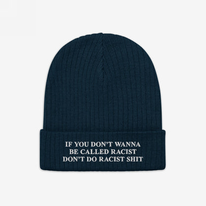 Anti-Racist Hat: A dark blue, rib-knit beanie with a folded cuff, featuring a bold white slogan challenging racism, embodying a statement of truth and action against discrimination.