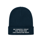 Anti-Racist Hat: A dark blue, rib-knit beanie with a folded cuff, featuring a bold white slogan challenging racism, embodying