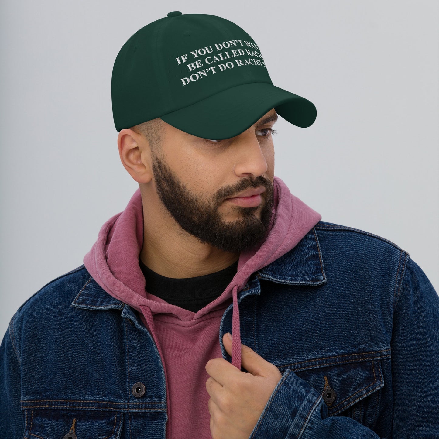 Young man wearing the Anti-Racist Hat, featuring a bold embroidered message challenging racism. The cap is styled with a pink hoodie and denim jacket, capturing the store’s advocacy for equality and justice.