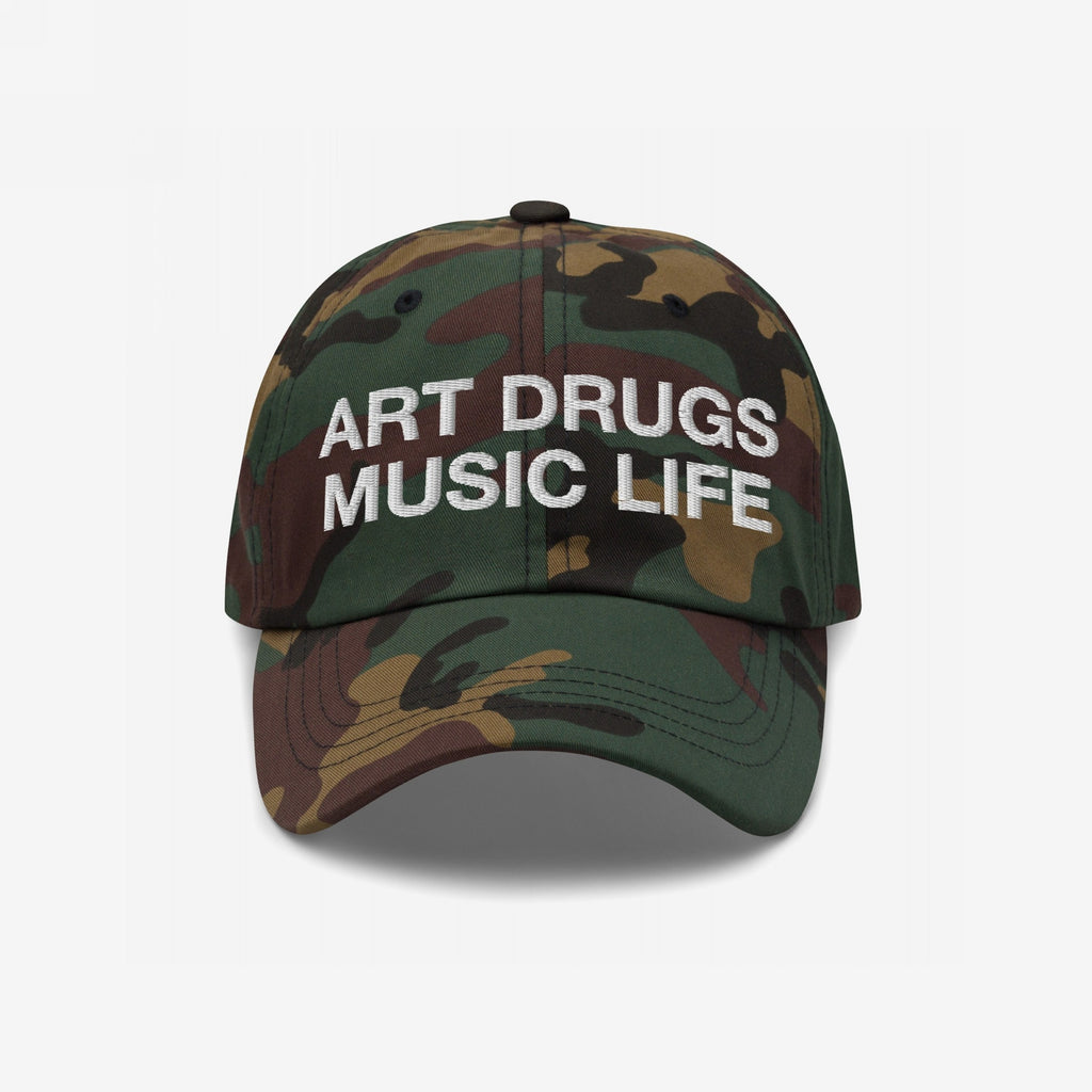 Art Drugs Music Life Hat: A woodland camo baseball cap featuring bold white embroidery of ART DRUGS MUSIC LIFE, symbolizing a creative, unapologetic spirit. Sturdy cotton with a curved brim and adjustable fit.