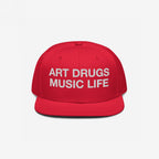 Bright red snapback hat with white text: ART DRUGS MUSIC LIFE, capturing a bold artistic manifesto for creativity and chaos enthusiasts. Ideal for artistic expression and unapologetic lifestyles.