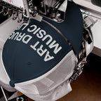 Art Drugs Music Life Hat in an embroidery machine. The navy trucker cap showcases bold white lettering, embodying a creative manifesto for those who embrace art, chaos, and sound.