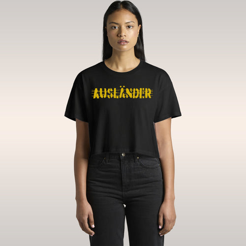 The Ausländer Women's Baby Tee features bold, yellow AUSLÄNDER text visually crossed out on a black, cropped T-shirt, embod