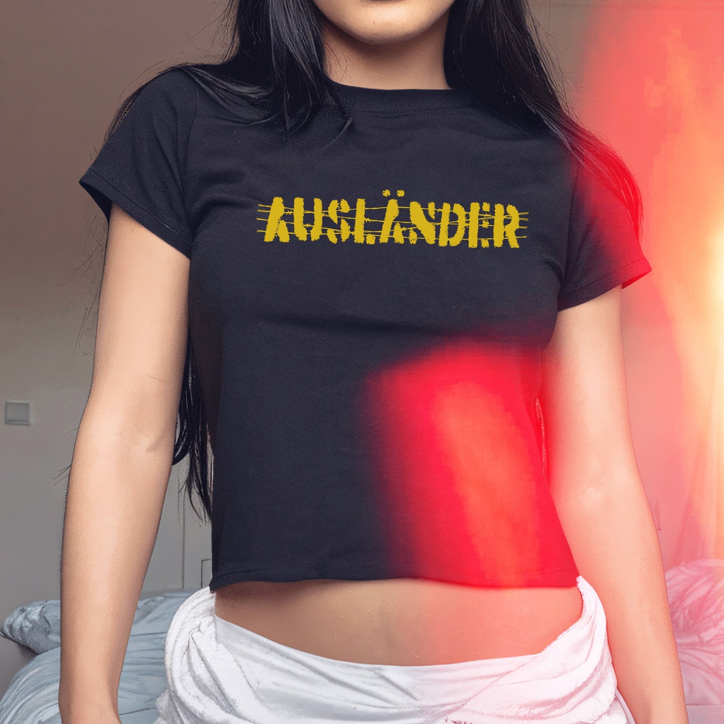 Ausländer Women's Baby Tee worn by a person indoors, featuring AUSLÄNDER strikethrough text on a black cropped T-shirt, paired with a white wrap around the hips, embodying bold, protest fashion.