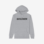 Light-heather gray Ausländer Hoodie with black glitch-style AUSLÄNDER. graphic, front kangaroo pocket, and drawstring hood. Bold statement on identity and presence, reflecting empowerment and individuality.