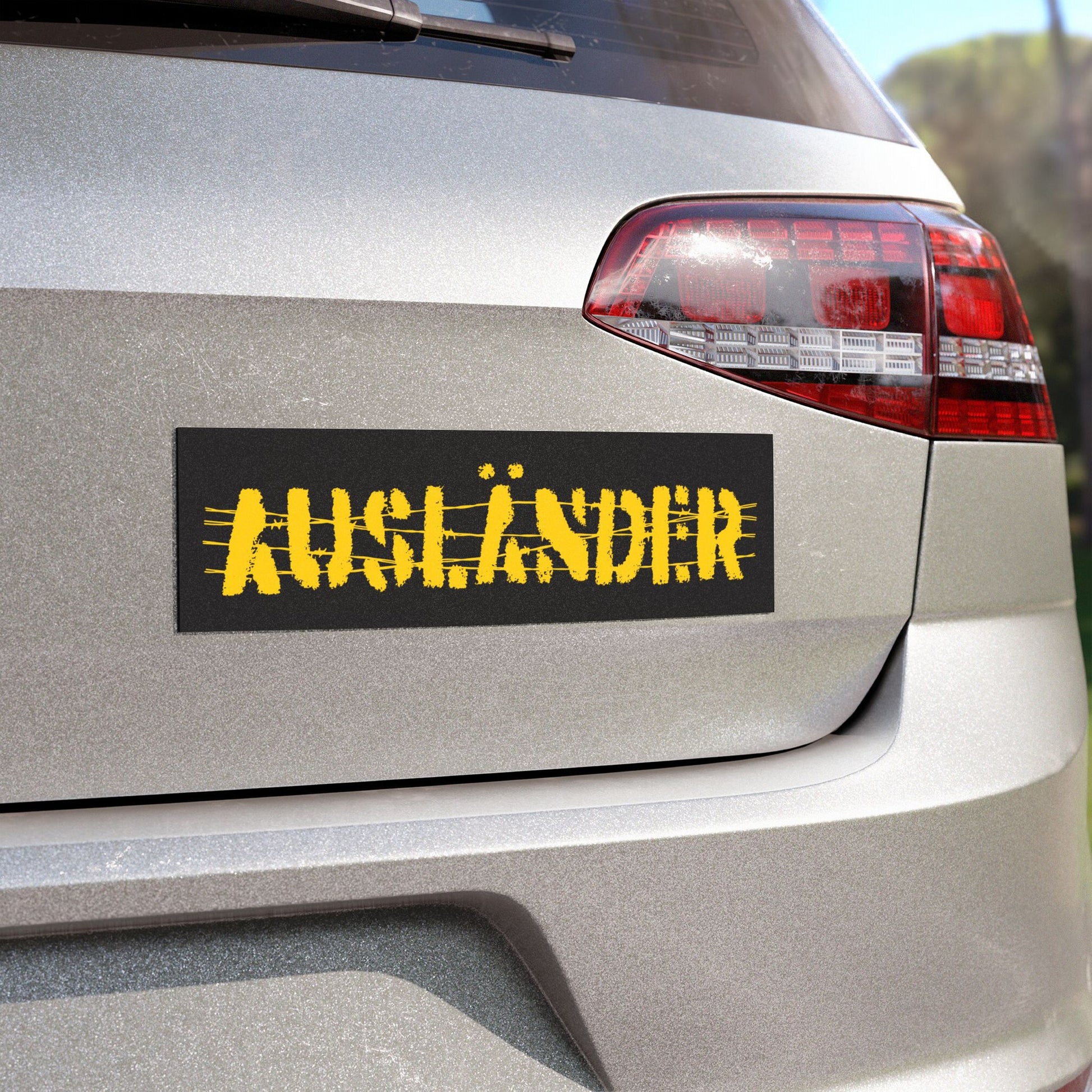 Auslander Sticker & Magnet on a hatchback's tailgate features the word “AUSLÄNDER” with barbed-wire lines, symbolizing resistance against nationalism and solidarity with immigrant struggles. Ideal for activists and expats.