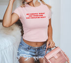 Young woman wears Be Careful Women's Baby Tee, a pale-pink crop top with bold red lettering, styled with ripped denim shorts and a small pink handbag, embodying a stylish and powerful message.