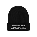 Black rib-knit cuffed beanie featuring white embroidery with the text Be Careful What You Wish For You Could Be Next, alignin