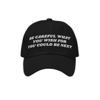 Black Be Careful Hat with white embroidered warning: “BE CAREFUL WHAT YOU WISH FOR YOU COULD BE NEXT”, embodying a bold p