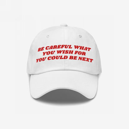 White baseball-style cap with red embroidered text, “BE CAREFUL WHAT YOU WISH FOR YOU COULD BE NEXT,” embodying a bold message. The Be Careful Hat offers a subtle yet assertive statement.
