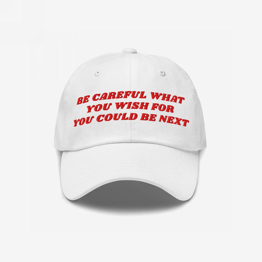 White baseball-style cap with red embroidered text, “BE CAREFUL WHAT YOU WISH FOR YOU COULD BE NEXT,” embodying a bold message. The Be Careful Hat offers a subtle yet assertive statement.