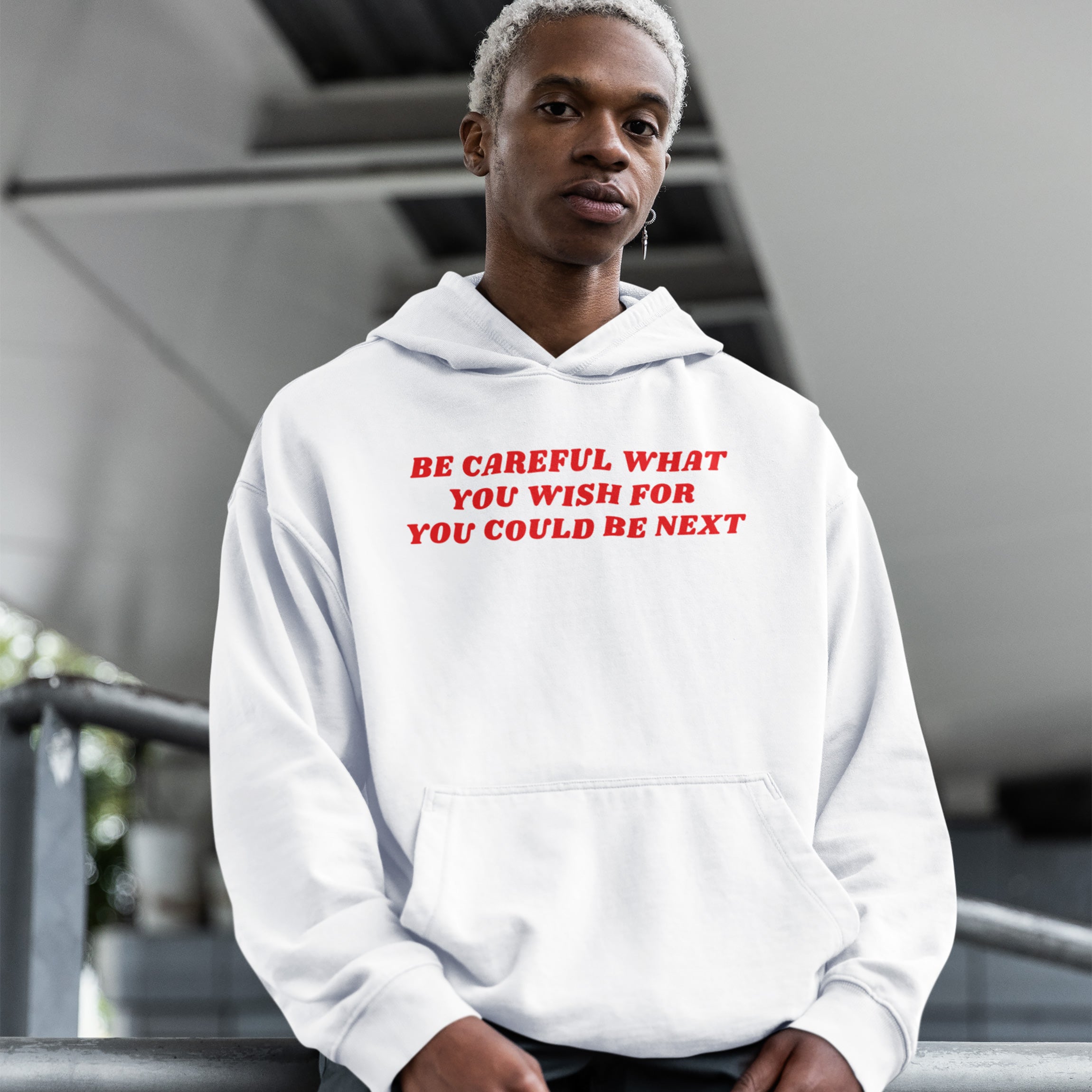 Young person outdoors in a white Be Careful Shirt hoodie, featuring bold red text warning against authoritarian ideologies. A powerful statement piece, combining Y2K flair with a message supporting equality and justice.