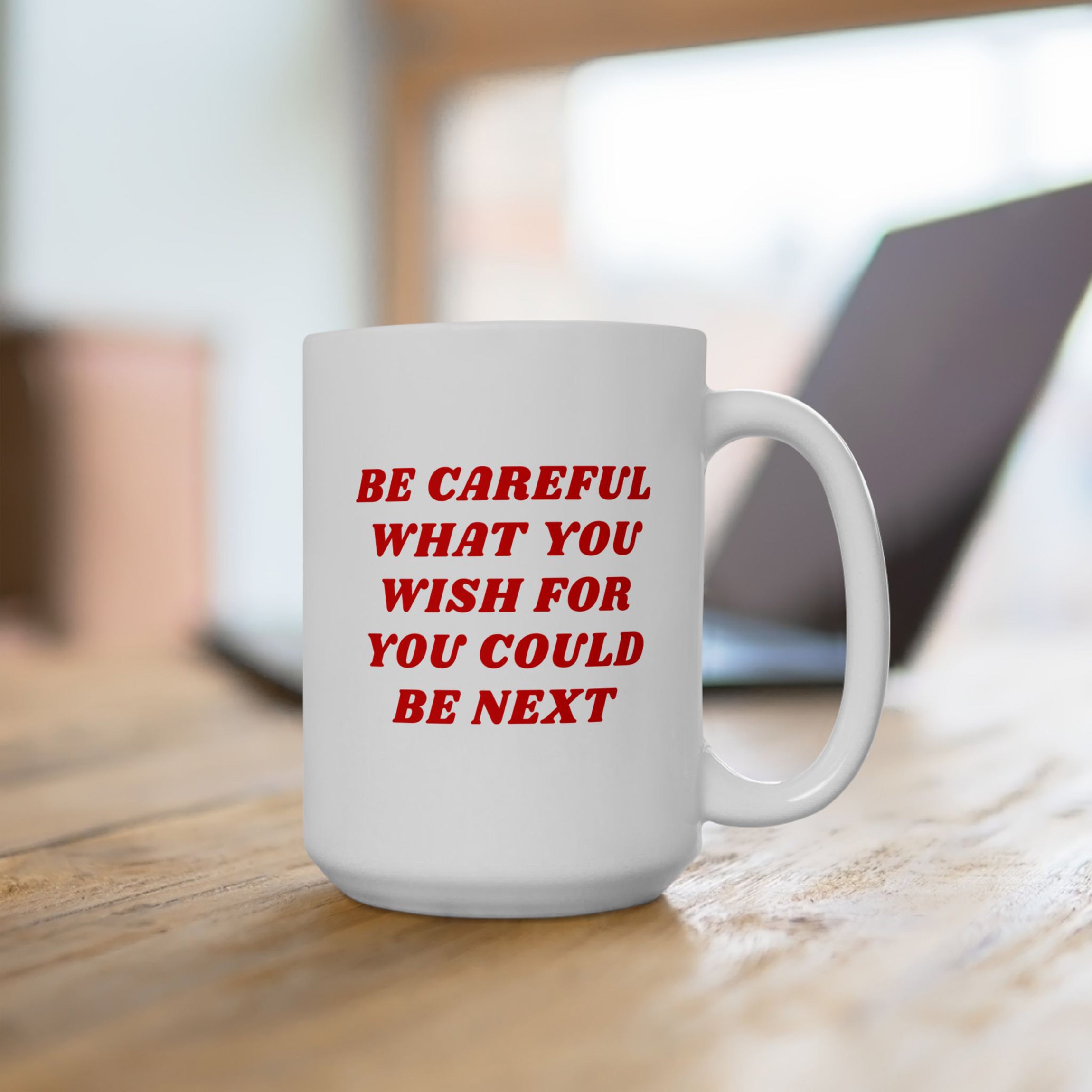 White ceramic Be Careful Mug on a wooden table, featuring bold red text. Ideal for progressives, this mug embodies activism and awareness, aligning with anti-fascist, equality-supporting values. Available in 11 oz and 15 oz sizes.