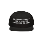 Black flat-brimmed snapback hat with BE CAREFUL WHAT YOU WISH FOR YOU COULD BE NEXT embroidered in white, embodying a bold po
