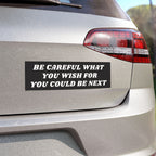 The image shows the Be Careful Sticker & Magnet on a silver car's trunk, featuring bold white text on a black background, conveying a thought-provoking message about vigilance and societal awareness.