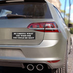 Rear view of a silver hatchback featuring the Be Careful Sticker & Magnet on the tailgate, emphasizing a bold message. Dual exhausts and partial taillight visible, promoting awareness and equality.