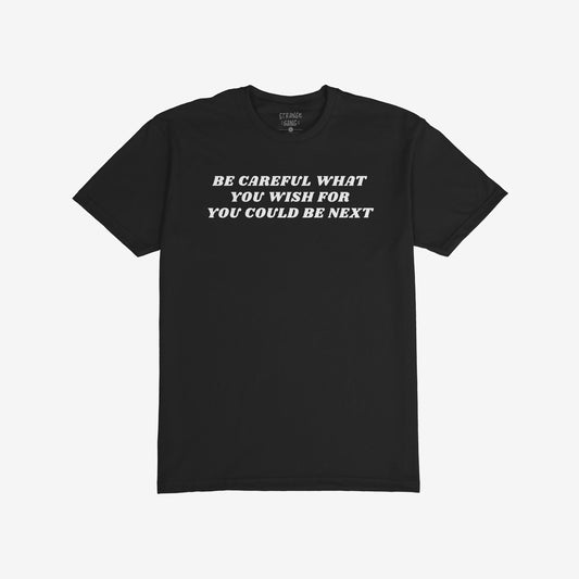 Black crew-neck Be Careful T-shirt featuring bold white text warning against authoritarianism, with a small label inside the collar. Designed for those challenging power structures. Available in various styles and sizes.