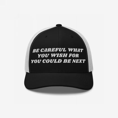 Black-and-white trucker cap featuring Be Careful What You Wish For – You Could Be Next embroidered text, conveying a bold message for those challenging the status quo. Supports Amnesty International.