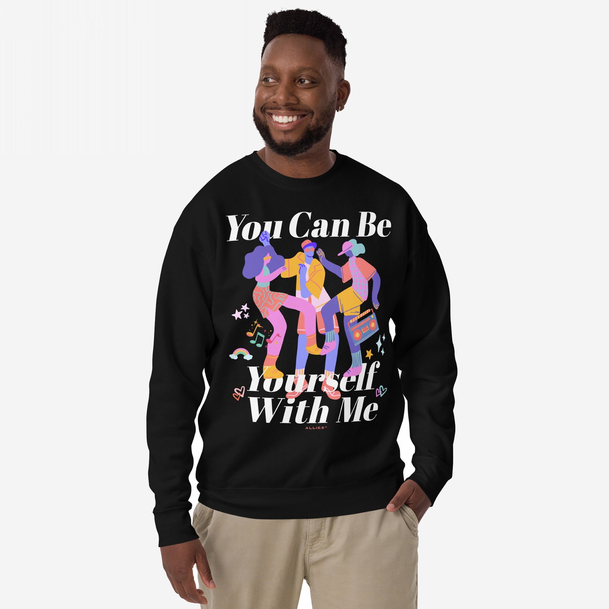 Smiling man wears the Be Yourself Sweatshirt, featuring a vibrant graphic of three dancing figures with musical elements and bold text: “You Can Be Yourself With Me,” symbolizing love and authenticity.