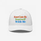 The Be Yourself Hat features a white trucker-style cap with bold embroidery that reads, You Can Be Yourself With Me, embodying inclusivity and self-expression with vibrant lettering.