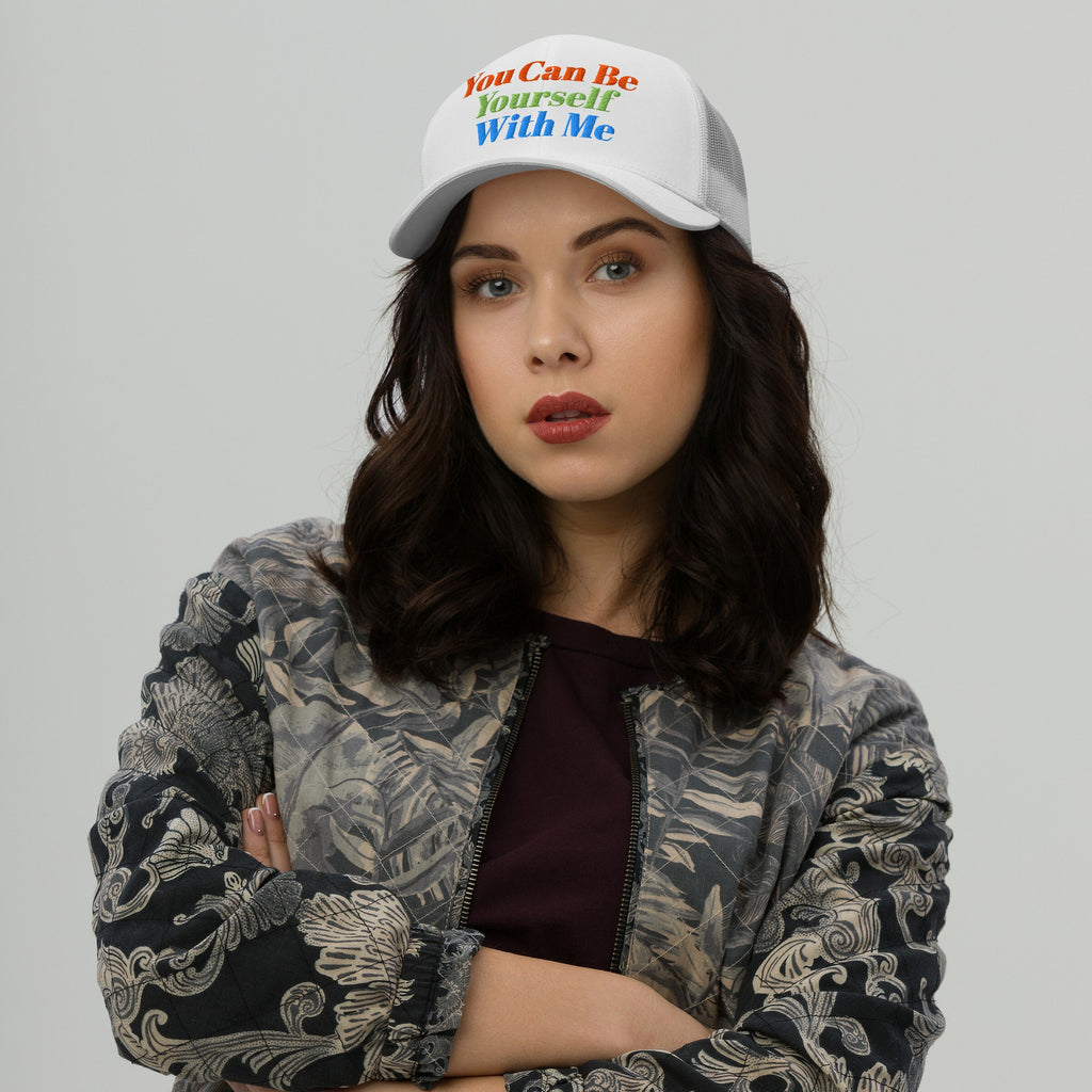 Young adult wearing the Be Yourself Hat, a white mesh-back baseball cap with rainbow embroidery reading “You Can Be Yourself With Me,” embodying inclusive and supportive values through vibrant messaging.