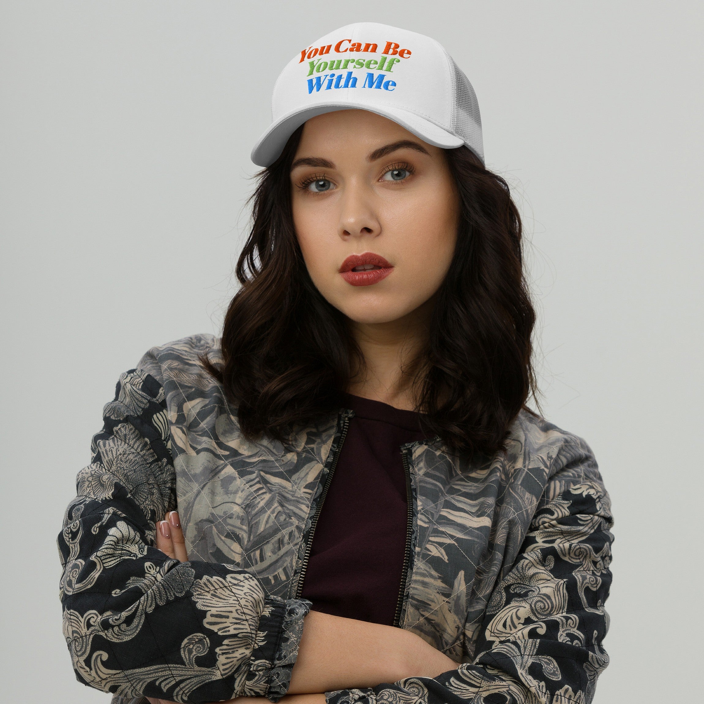 Young adult wearing the Be Yourself Hat, a white mesh-back baseball cap with rainbow embroidery reading “You Can Be Yourself With Me,” embodying inclusive and supportive values through vibrant messaging.