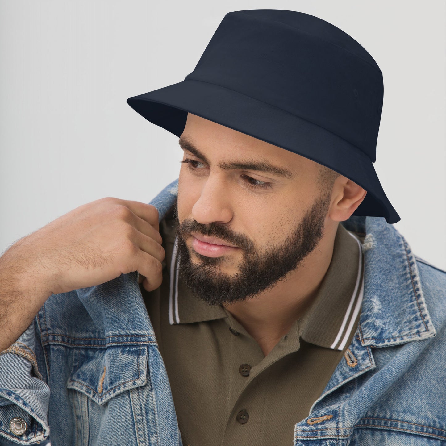 A man wears a navy-blue Bucket Hat In Custom Colors with an embroidered protest design, styled with an olive polo and denim jacket, embodying a bold, progressive statement.