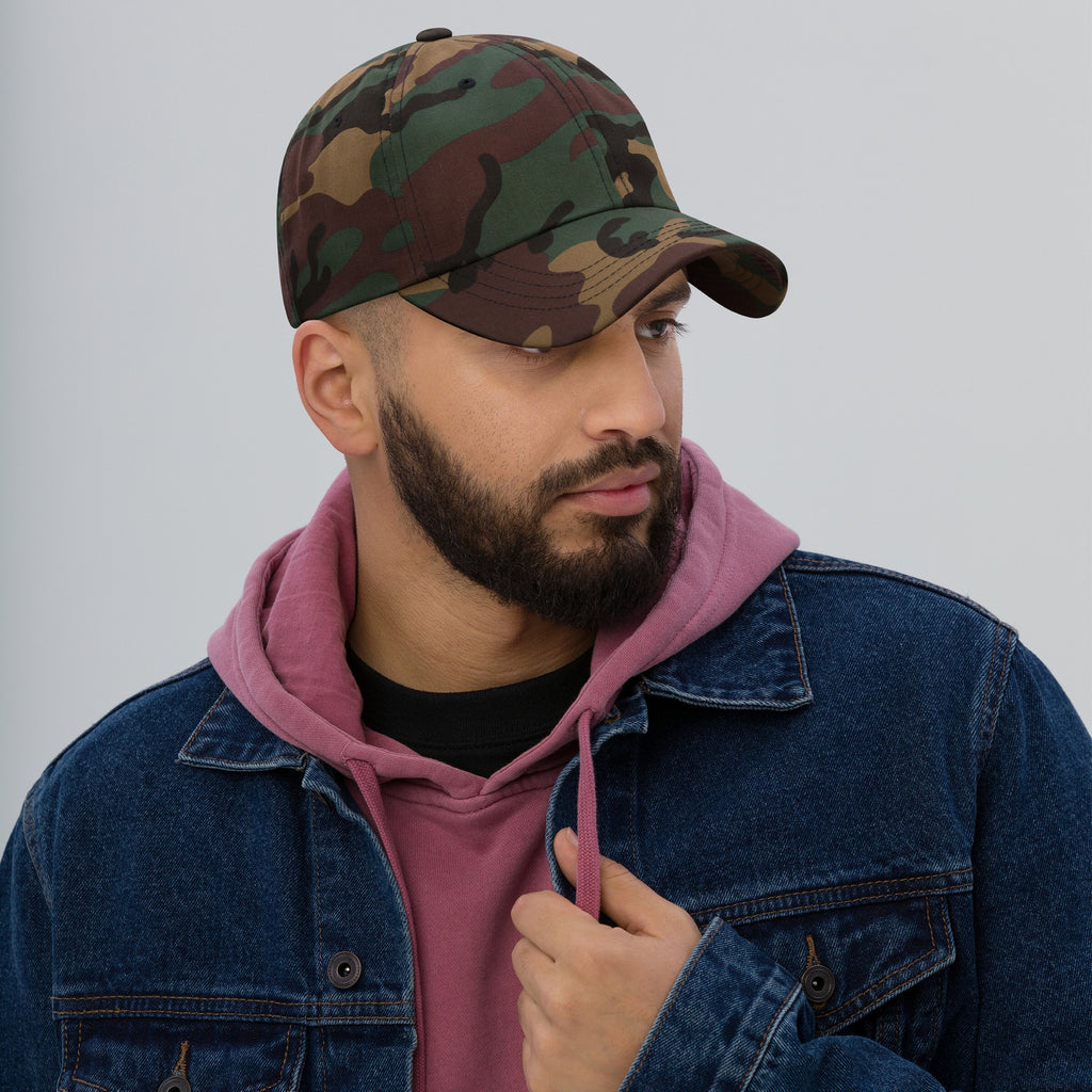 Young man in woodland-camo Dad Hat In Custom Colors, showcasing an unstructured design. He pairs it with a denim jacket and hoodie, embodying a laid-back, activist style.