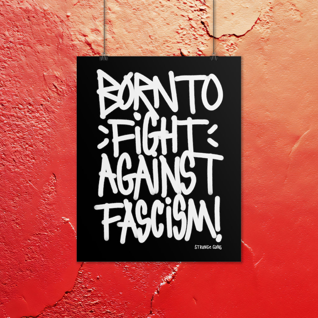 Born To Fight Against Fascism Graffiti Poster displays bold, white graffiti text on a black background, mounted on a textured red wall. Signature tag in the corner, embodying defiance and street protest energy.