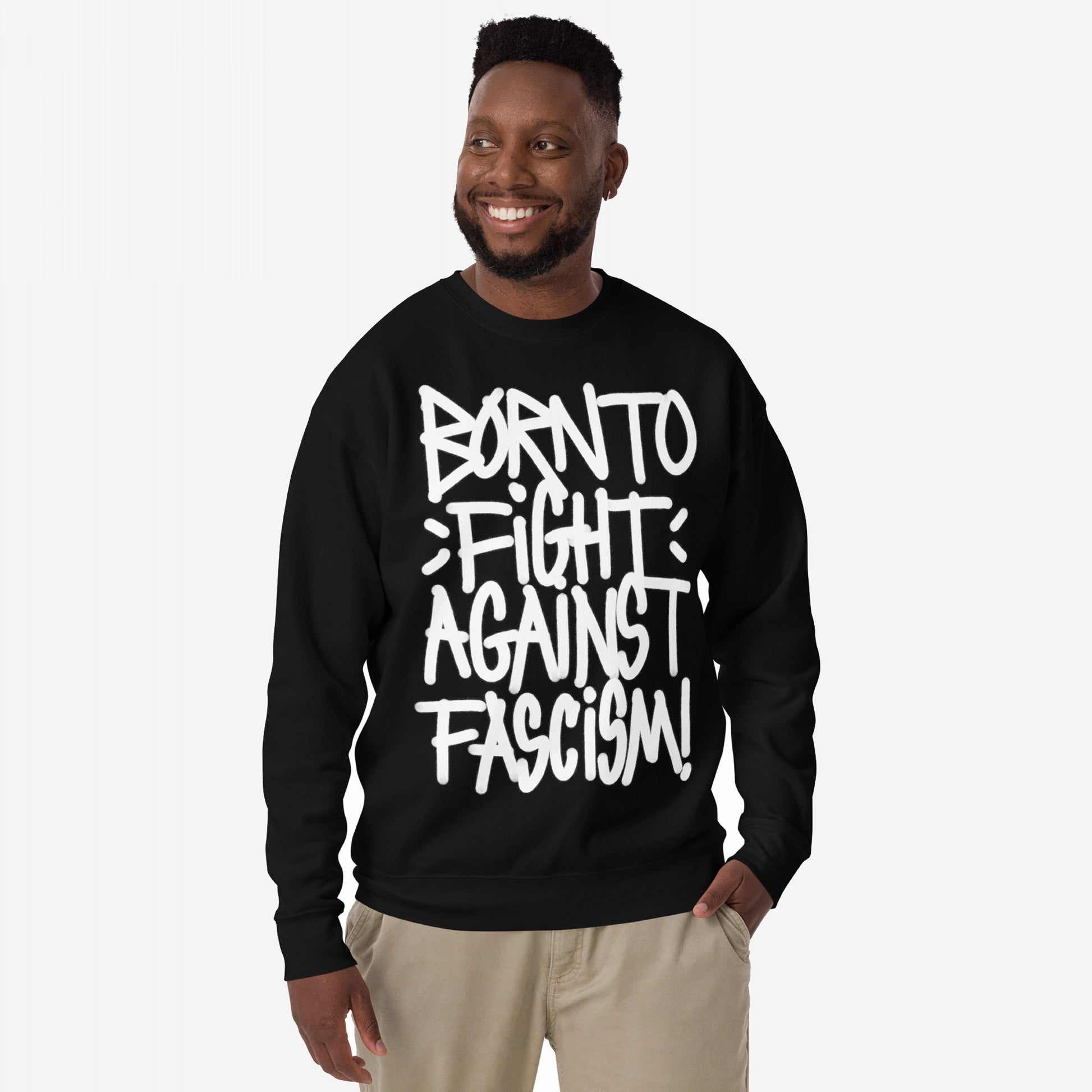 Smiling Black man wearing the Born To Fight Against Fascism Graffiti Hoodie & Sweatshirt with bold white graffiti-style text, light-khaki pants, embodying defiance and rebellion.