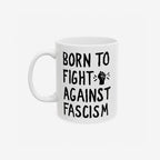 White ceramic mug with bold black slogan BORN TO FIGHT AGAINST FASCISM and a stylized raised-fist graphic, emphasizing progressive resistance. Available in 11 oz. and 15 oz., supporting ACLU.