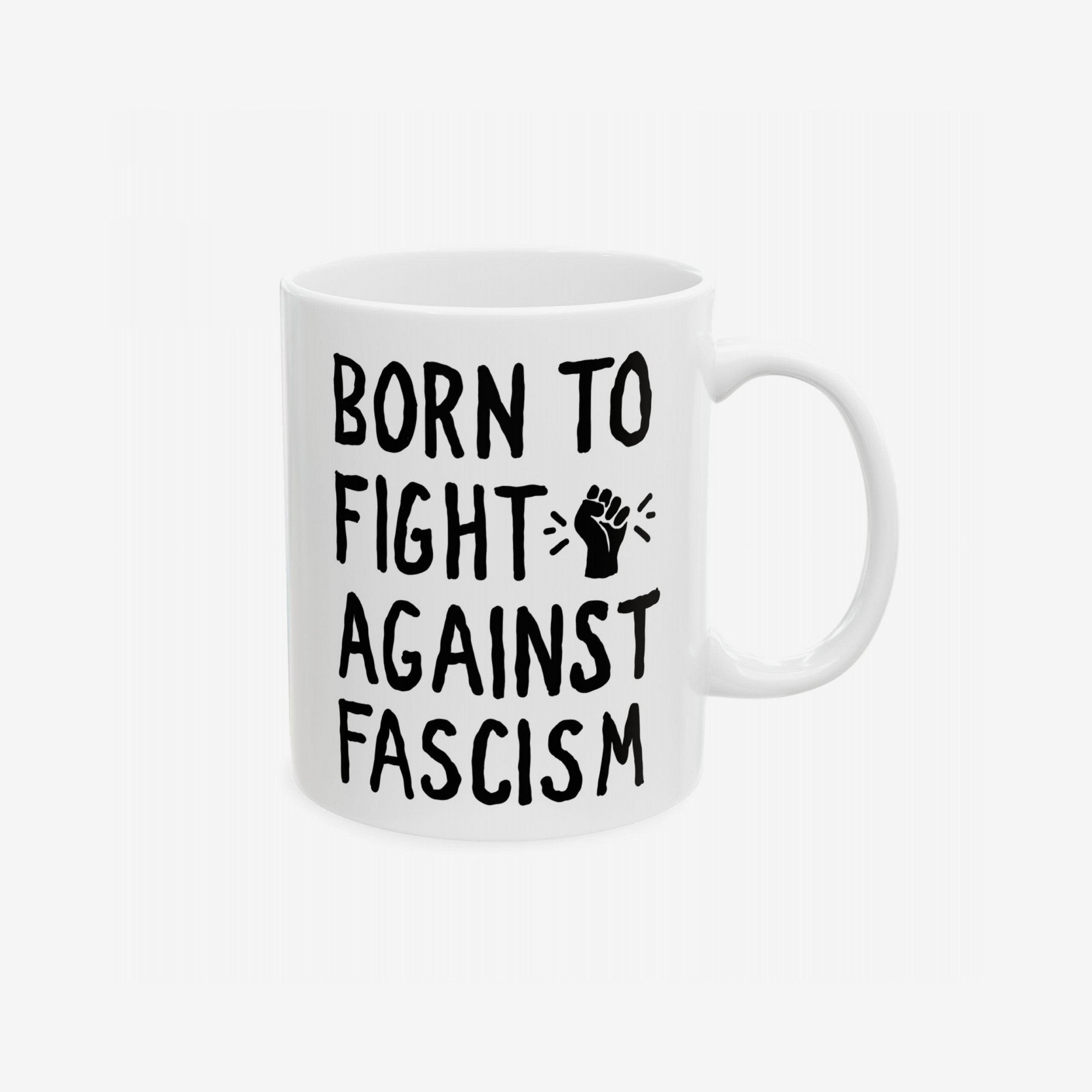 White ceramic mug featuring BORN TO FIGHT AGAINST FASCISM in bold black letters, with a small raised fist graphic, embodying progressive activism and everyday resistance. Available in two sizes, supporting the ACLU.