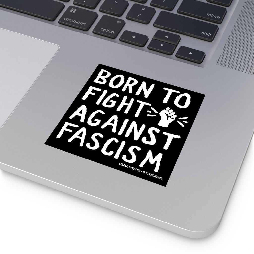 Silver laptop corner with a Born To Fight Against Fascism sticker, featuring hand-drawn lettering and a clenched fist graphic near the trackpad, symbolizing resistance and empowerment.