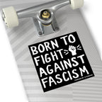 The underside of a skateboard features the Born To Fight Against Fascism sticker with hand-drawn lettering and a raised fist, symbolizing resistance and equality.