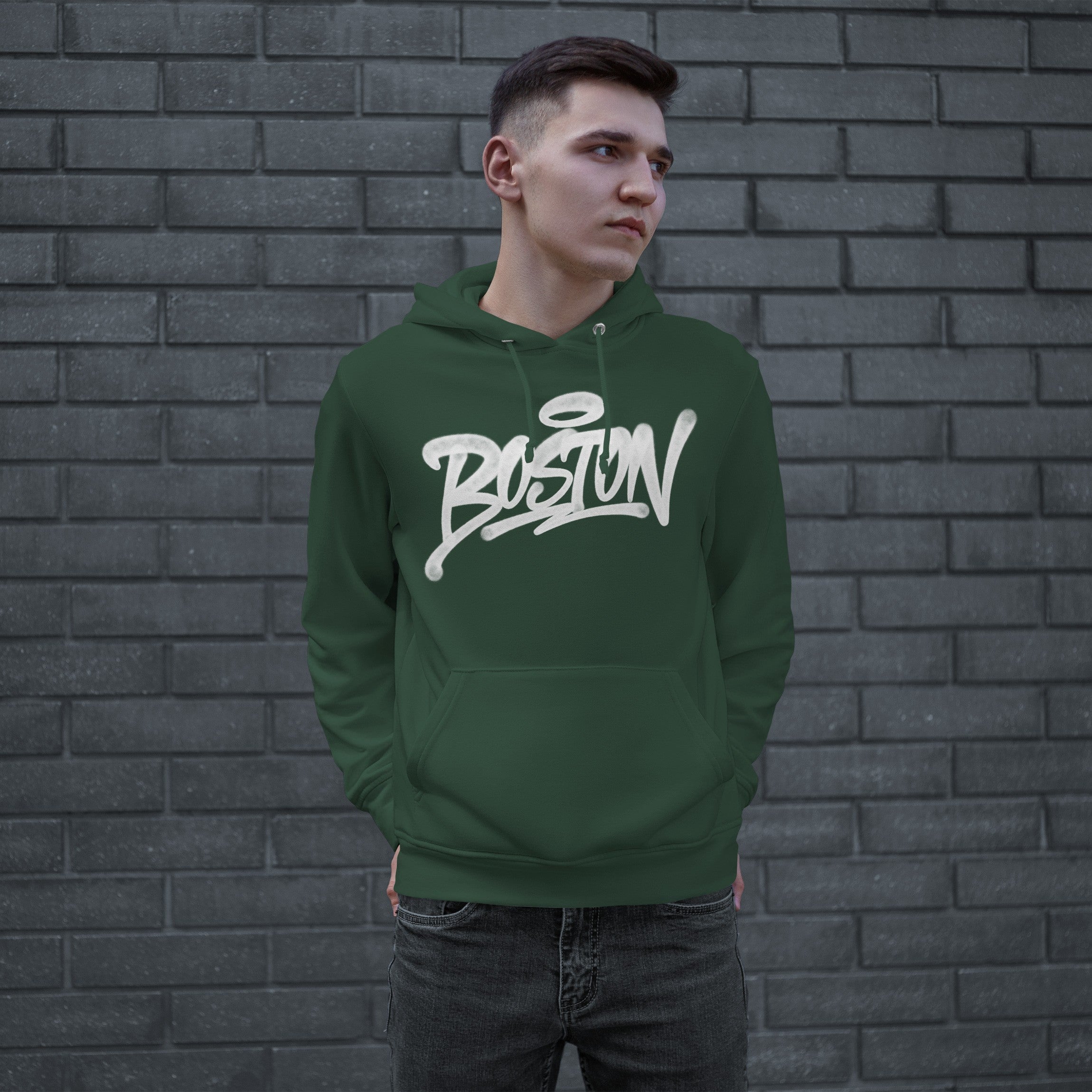 Young person in a forest-green Boston Handstyle Hoodie, featuring a white graffiti-style logo, stands against a brick wall, hands in kangaroo pocket, embodying the city's bold, authentic spirit.