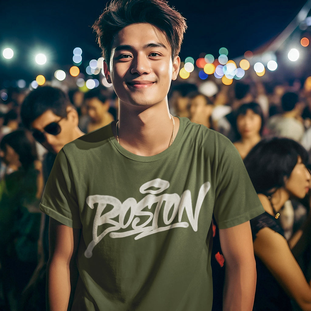 Young man at a lively evening event wears a Boston Handstyle T-shirt with stylized graffiti lettering, embodying the city's spirit amidst a festive, twinkling backdrop.