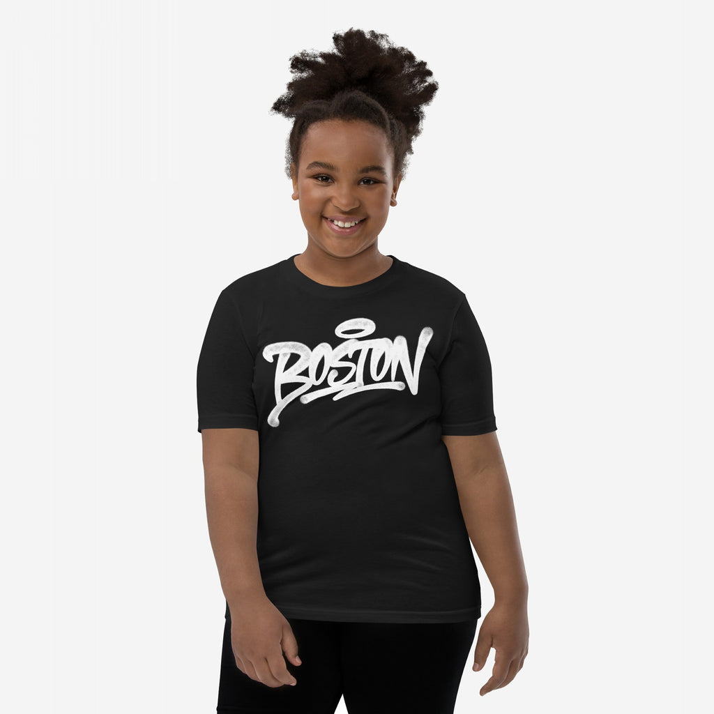 Young child smiling, wearing a fitted black Boston Handstyle T-shirt with bold white graffiti-style script, against a plain background. The T-shirt embodies a vibrant, non-touristy Boston statement.