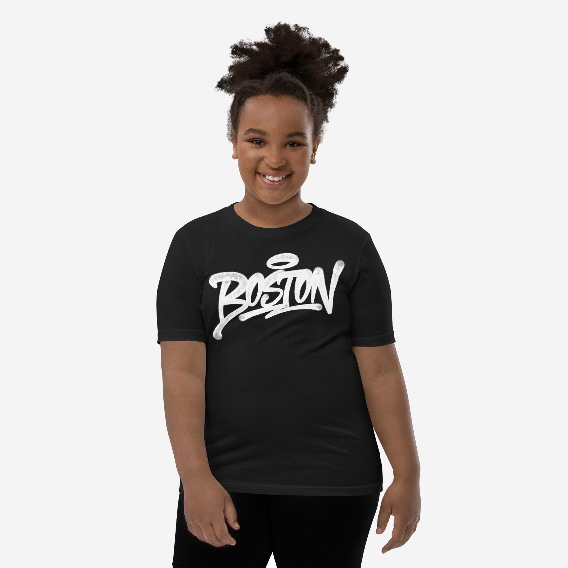 Young child smiling, wearing a fitted black Boston Handstyle T-shirt with bold white graffiti-style script, against a plain background. The T-shirt embodies a vibrant, non-touristy Boston statement.
