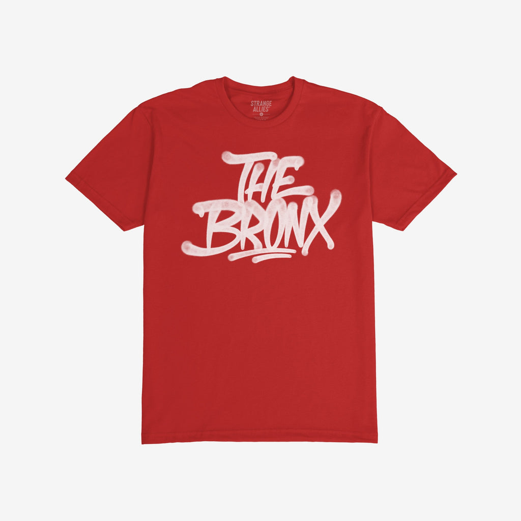 Bronx Handstyle T-shirt features bold “THE BRONX” graffiti in white spray-paint lettering on a red tee, capturing raw borough pride and urban spirit. Brand “STRANGE ALLIES” visible inside the collar.
