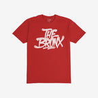 Bronx Handstyle T-shirt features bold “THE BRONX” graffiti in white spray-paint lettering on a red tee, capturing raw borough pride and urban spirit. Brand “STRANGE ALLIES” visible inside the collar.