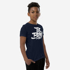Young boy in a navy Bronx Handstyle T-shirt featuring white graffiti-style The Bronx print, standing with one hand in his pocket against a plain white backdrop.
