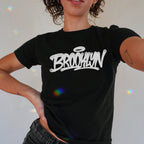 Brooklyn Handstyle Women's Baby Tee showcases bold graffiti-style BROOKLYN lettering with a halo, embodying street art culture. The black tee's Y2K cut offers versatile styling with rainbow light accents.
