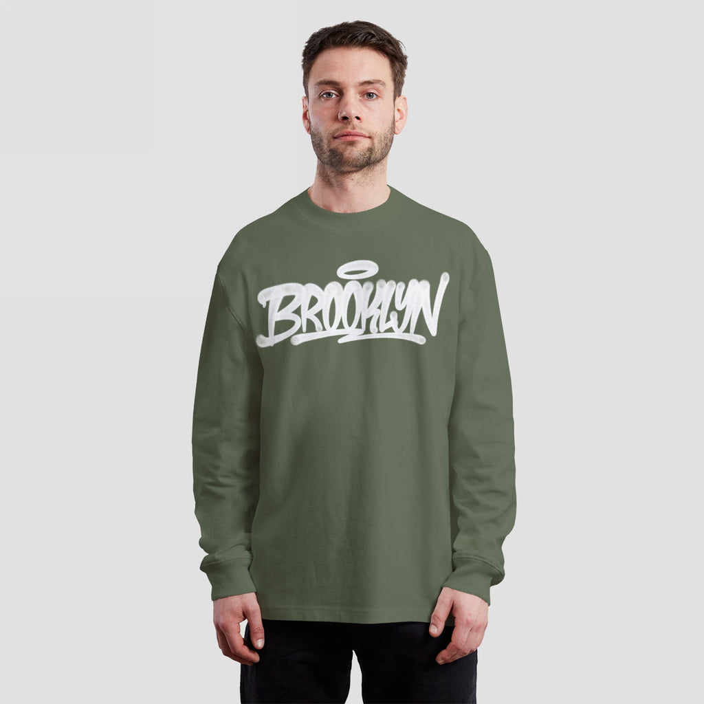 Young man in olive-green Brooklyn Handstyle T-shirt, featuring bold white graffiti lettering, epitomizing everyday borough pride and cultural roots, perfect for diverse activities and expressing individual beliefs.